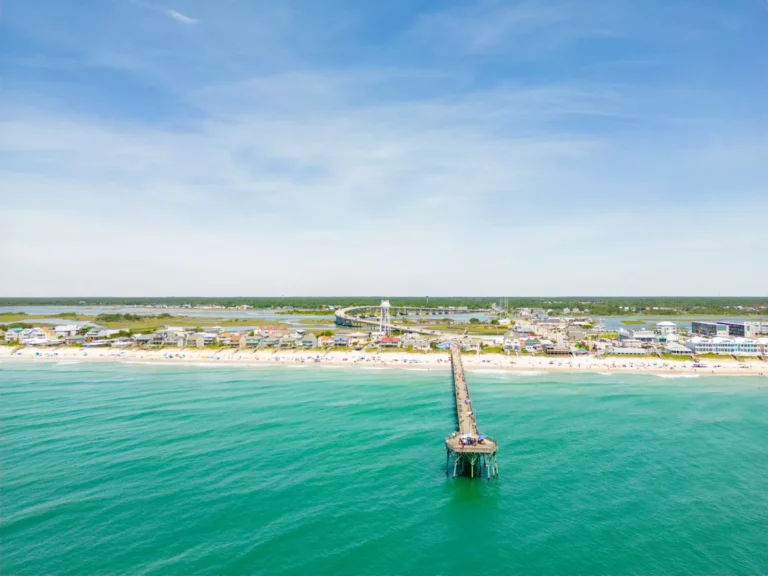 Surf City Pier - image of pier extending out into a teal colored ocean with blue sky and light wispy clouds highlighting a vibrant ocean front community